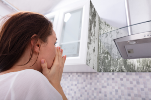A picture of a woman with her hands over her mouth looking at mold on her wall next to her cabinets in New Orleans, LA